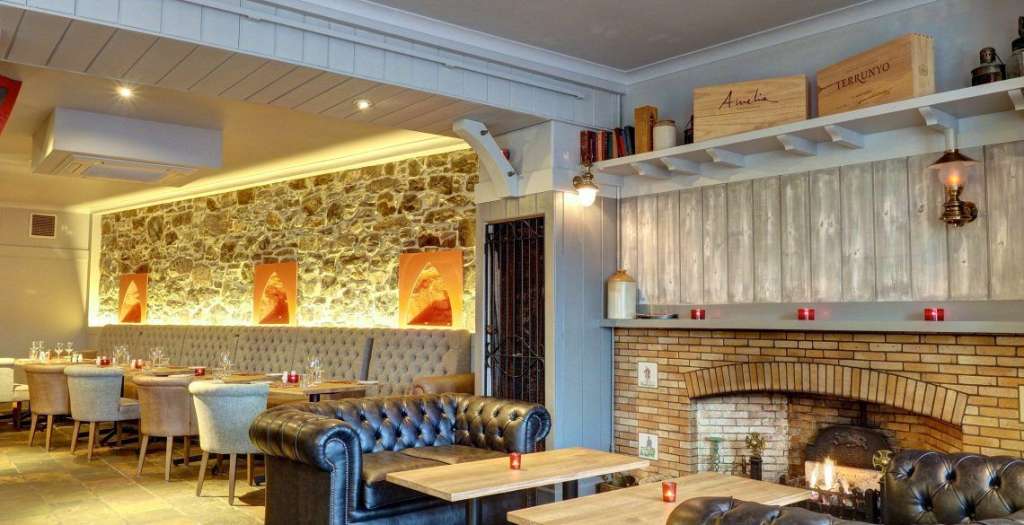 Das Bild zeigt das Innere eines Restaurants mit einer Steinwand, einem Kamin und Sitzbereichen.