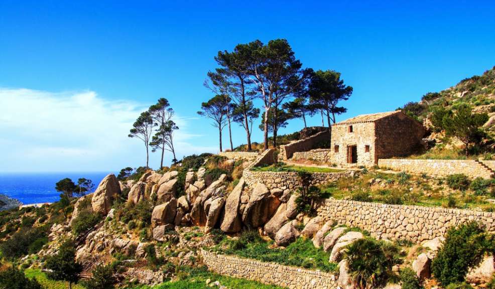 Ein Steinhaus auf einem felsigen, begrünten Hügel mit Blick auf das Meer.