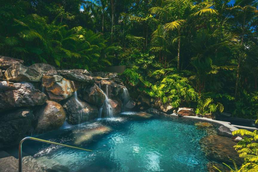 Ein kleiner Wasserfall fließt in einen türkisfarbenen Pool, der von üppiger tropischer Vegetation umgeben ist.