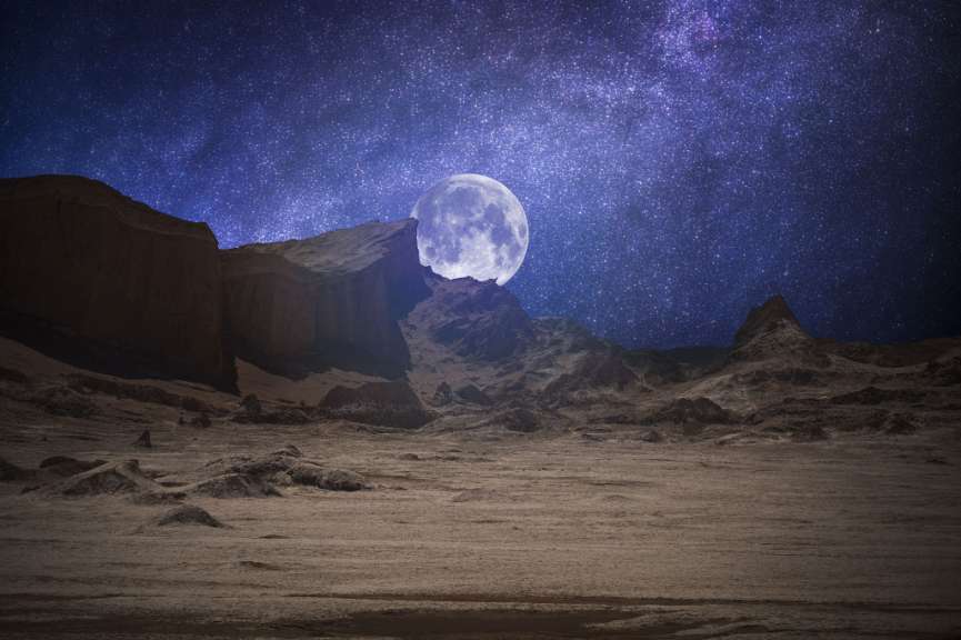 Ein voller Mond steigt über einer Wüste mit Bergen im Hintergrund