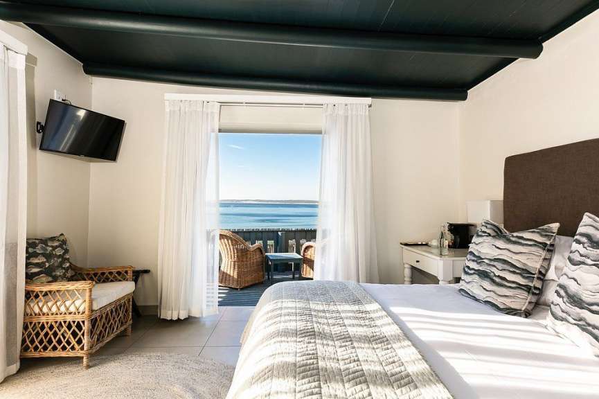 Ein Hotelzimmer mit Blick auf das Meer, komplett mit einem Bett, zwei Sesseln und einem Fernseher.