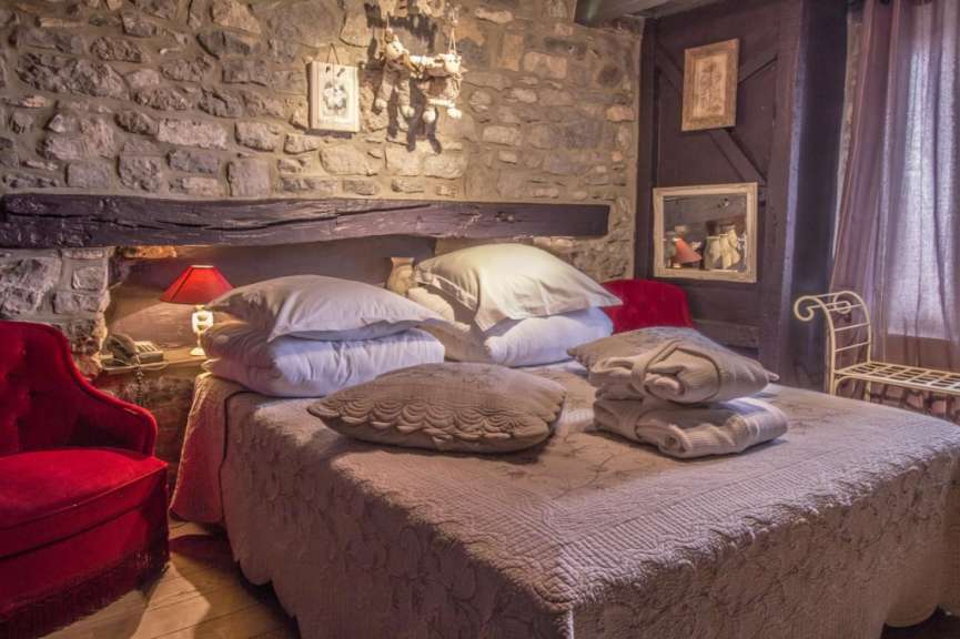 Ein Bett mit weißen Kissen und Decken, das mit einem roten Sessel und einer Steinwand dekoriert ist.