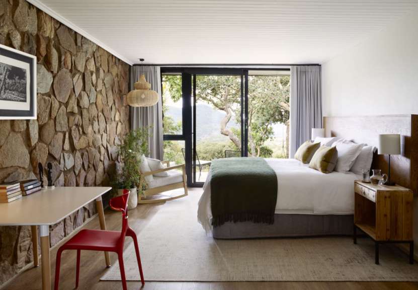Ein stilvolles Schlafzimmer mit einem Bett, einem Schreibtisch und einem großen Fenster mit Blick auf die Natur.