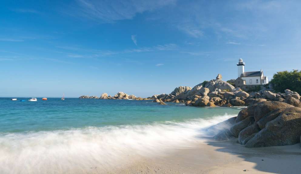 Ein Leuchtturm sitzt auf einem Felsen über einem Strand