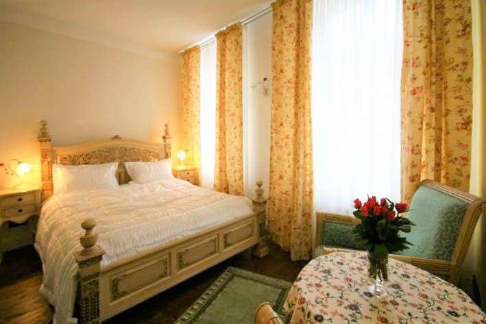 Ein Schlafzimmer mit einem großen Bett, floralen Vorhängen und einem kleinen Tisch mit einer Vase voller Rosen.