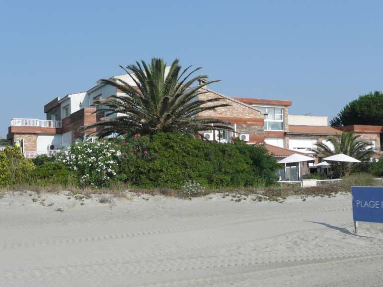 Ein blaues Schild steht auf einem Sandstrand in der Nähe eines großen Hauses