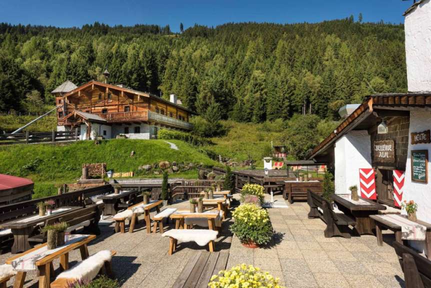Ein alpenländisches Gasthaus mit Terrasse und Bergwald im Hintergrund.