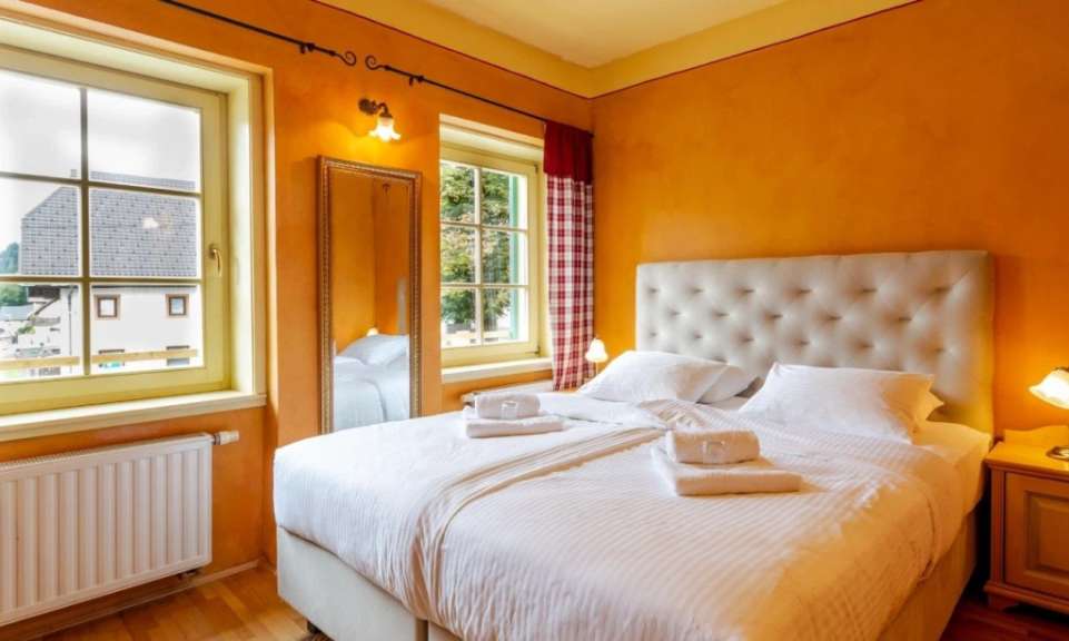 Ein Doppelbett mit weißen Laken und weißen Handtüchern steht in einem Zimmer mit orangefarbenen Wänden und einem großen Fenster.