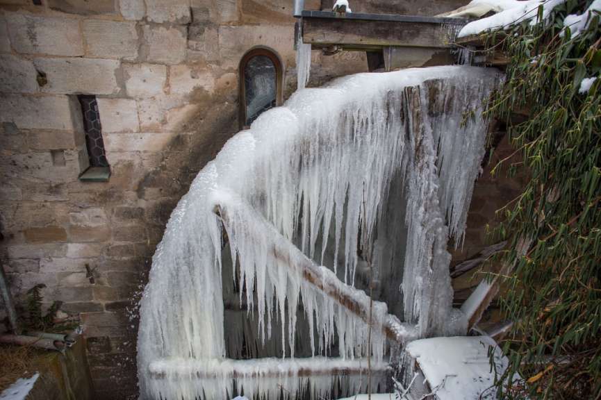 Eiszapfen hängen von einem Wasserrad in der Nähe eines Fensters