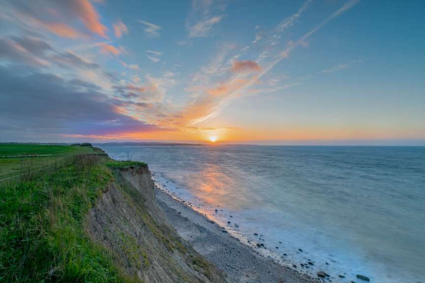 Ein Sonnenuntergang über dem Meer, mit einer Klippe im Vordergrund.