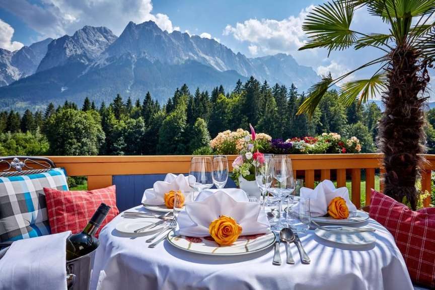 Ein Tisch mit Tellern und Gläsern auf einem Balkon mit Bergen im Hintergrund
