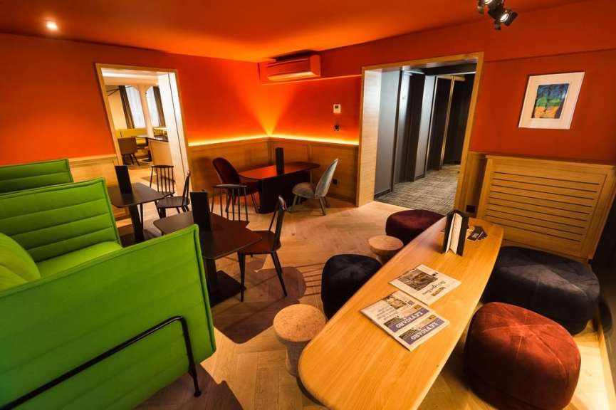 Das Bild zeigt einen stilvollen und modernen Lounge-Bereich mit leuchtend roten Wänden, grünen Polstermöbeln und Holztischen.