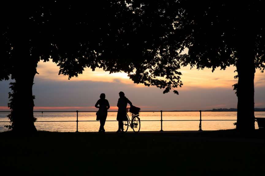 Eine Frau steht neben einem Mann mit einem Fahrrad bei Sonnenuntergang