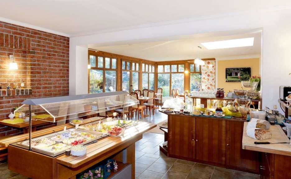 Eine Buffet-Anrichte mit Speisen und Getränken steht vor einer großen Fensterfront mit Tischen und Stühlen.
