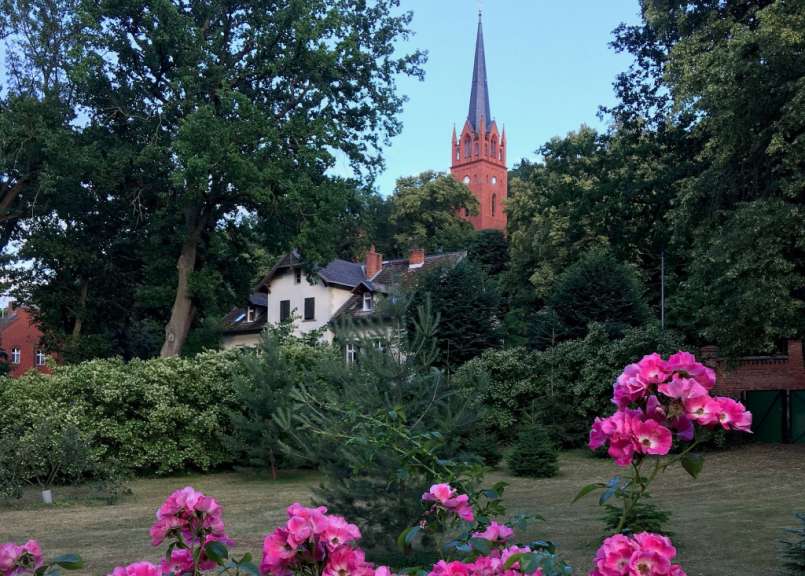 Eine rote Kirche steht hinter einem Garten mit rosa Blumen