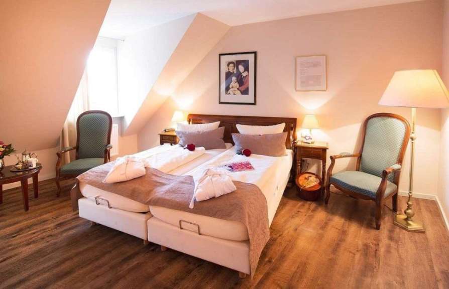Ein Doppelbett steht in einem Schlafzimmer mit zwei Stühlen, Nachttischen und einem Boden aus Holzplanken.