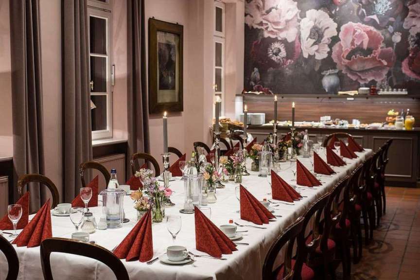Eine festlich gedeckte Tafel mit Kerzen und Blumen steht in einem Raum mit einer großen Wandmalerei von Blumen.