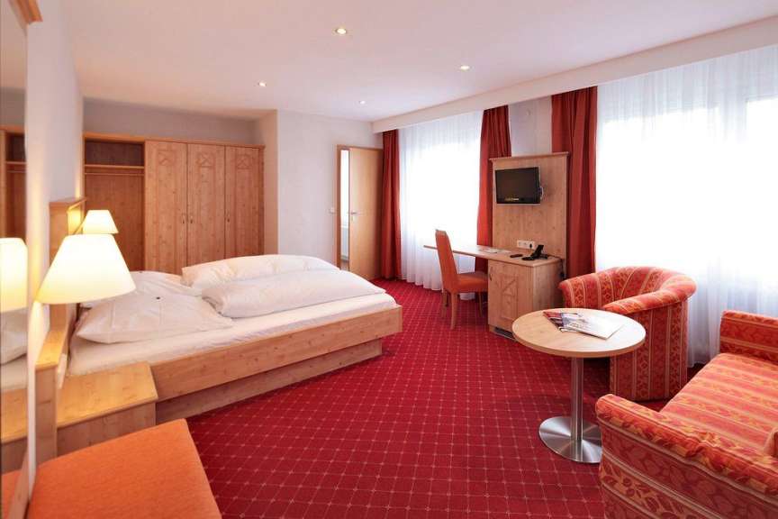 Dieses Bild zeigt ein Hotelzimmer mit einem großen Bett, einem Schreibtisch mit Stuhl und einer Sitzecke.