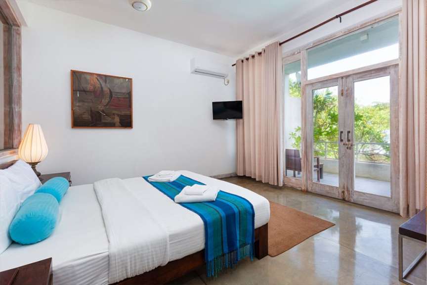 Ein modern eingerichtetes Schlafzimmer mit einem großen Bett und direktem Zugang zu einem Balkon mit Blick ins Grüne.