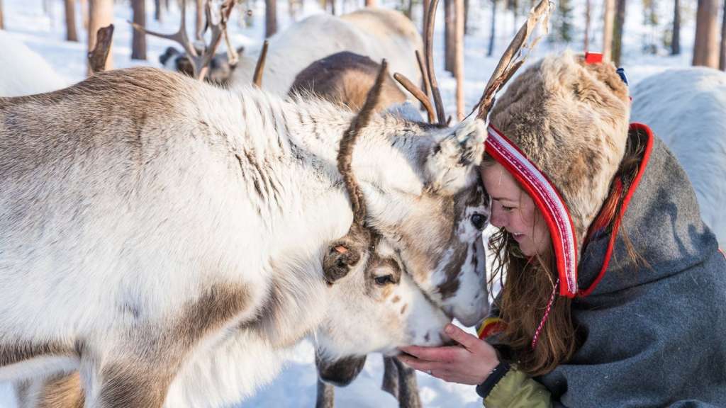 Eine Frau streichelt ein Rentier im Schnee