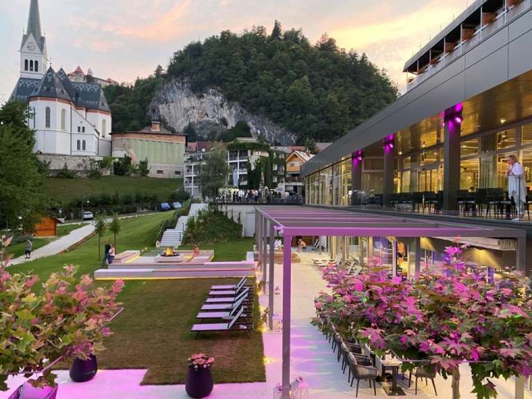 Eine Gruppe von Menschen sitzt auf einer Terrasse vor einem Gebäude mit einer Kirche im Hintergrund