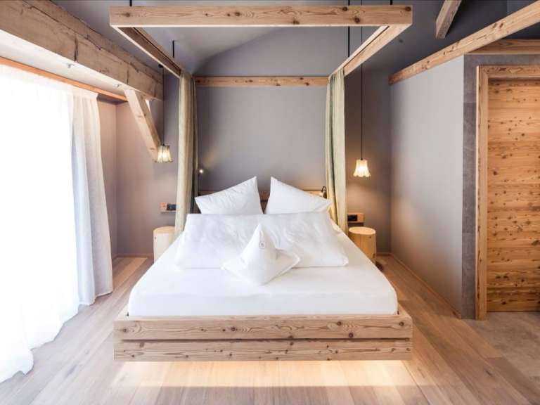Ein modern gestaltetes Schlafzimmer mit einem Himmelbett aus Holz und weißen Bettwäsche.