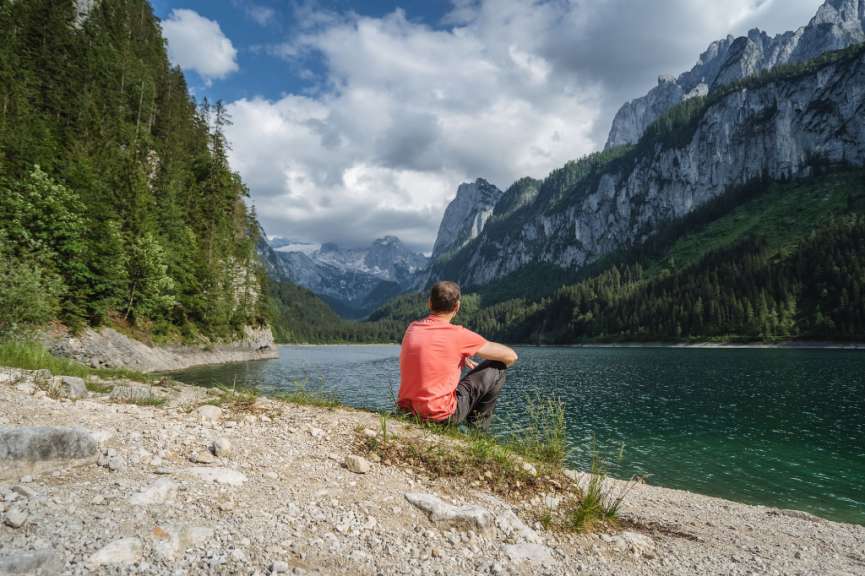 Ein Mann sitzt am Ufer eines Sees mit Bergen im Hintergrund
