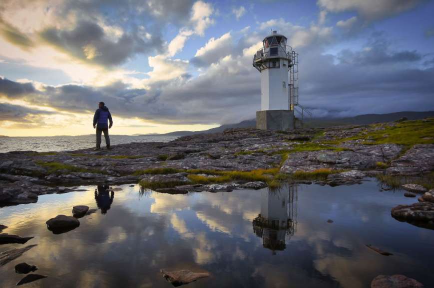 Ein Mann steht vor einem Leuchtturm und schaut auf das Meer