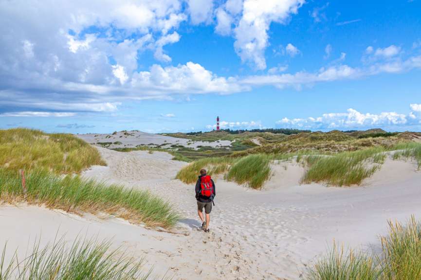 Ein Mann mit einem roten Rucksack geht durch die Dünen
