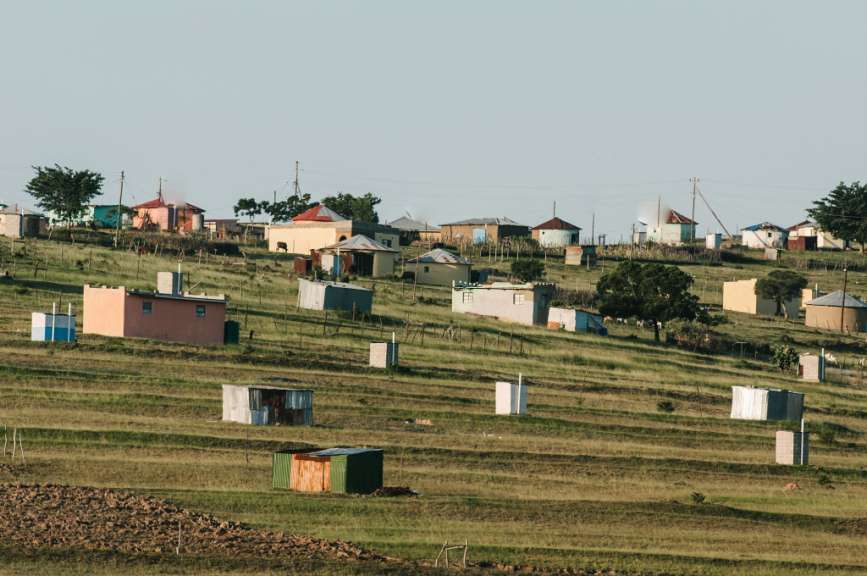 Auf einer grünen Hügellandschaft mit Terrassen sind kleine Häuser und Nebengebäude verteilt.