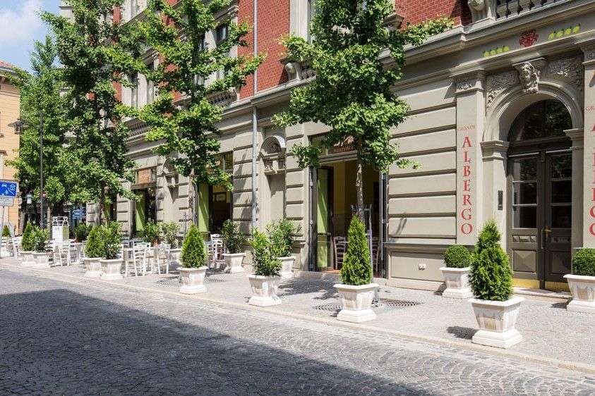 Ein Gebäude mit vielen Fenstern und Türen, das mit vielen Bäumen und Topfpflanzen geschmückt ist, steht neben einer Straße.