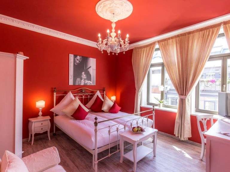 Ein rotes Schlafzimmer mit einem Himmelbett, einem Kronleuchter und roten Wänden.