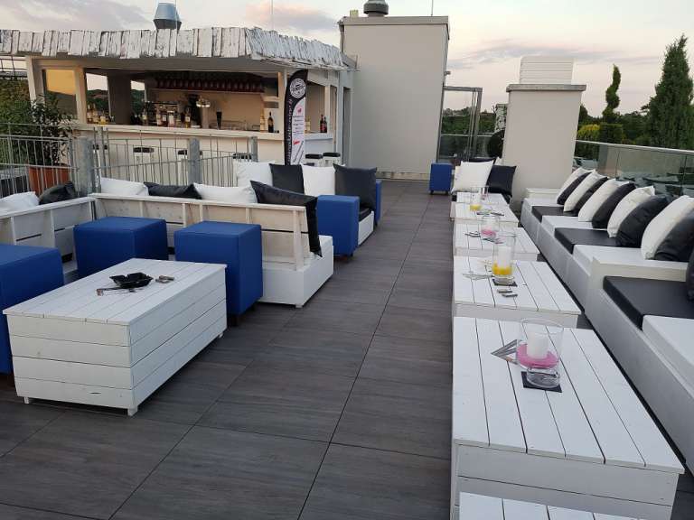 Eine Dachterrassen-Bar mit Sitzgelegenheiten und Tischen, dekoriert mit weißen und schwarzen Kissen, blauen Hockern, Kerzen und Aschenbechern.