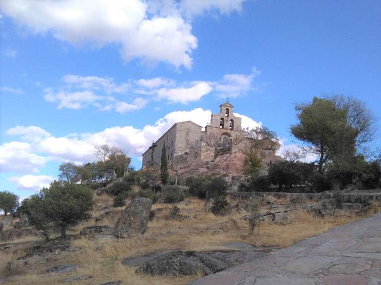 Ein Kloster thront auf einem felsigen Hügel unter einem blauen Himmel mit Wolken.