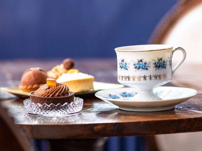 Eine weiße Tasse mit blauen Blumen darauf sitzt auf einem Tisch neben einem kleinen Kuchen