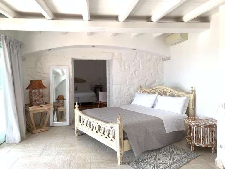 Ein Schlafzimmer mit einem weißen Bett mit grauer Decke und weißen Kissen, zwei Nachttischen, einem Spiegel und einer Wand mit Steindekoration.