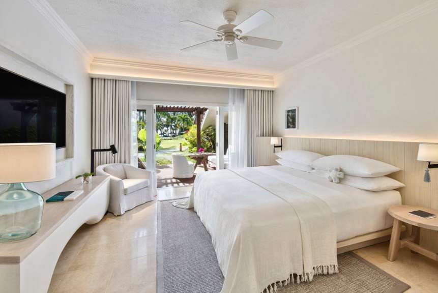 Ein luxuriöses Schlafzimmer mit einem großen Bett, weißen Möbeln und Blick auf einen tropischen Garten.