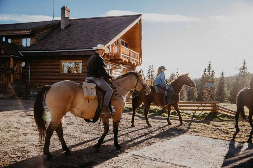 Ein Mann und eine Frau reiten Pferde vor einem Blockhaus