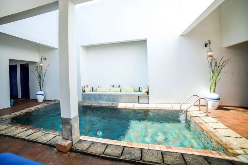 Ein Innenhof mit einem Pool, einer Sitzbank mit Kissen und einer Lampe.