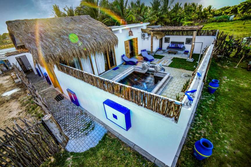 Das Bild zeigt eine luxuriöse Villa mit Strohdach und einem privaten Pool in einer tropischen Umgebung.