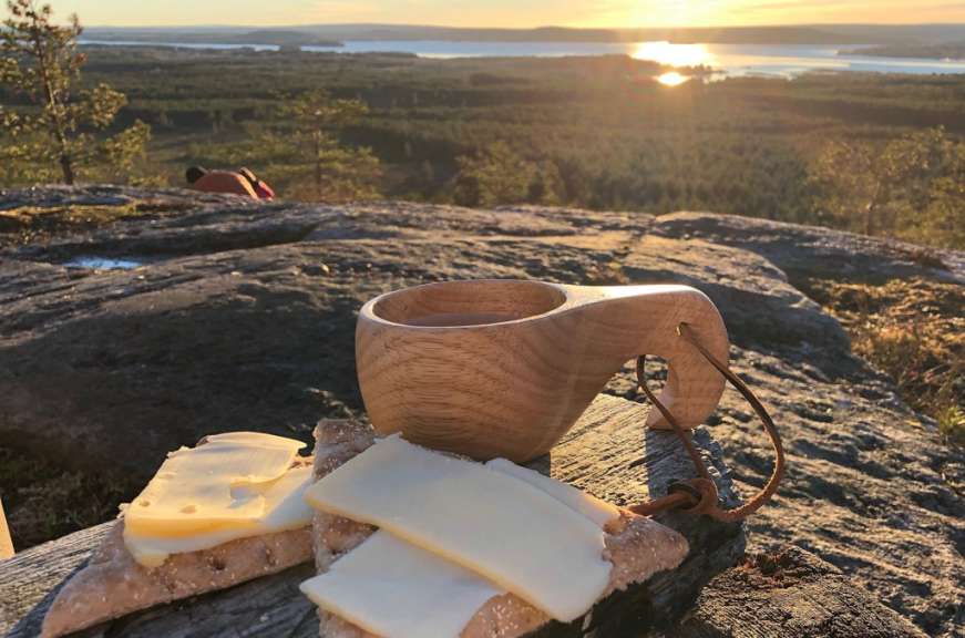 Eine Tasse Kaffee steht auf einem Felsen neben einem Stück Brot und Käse