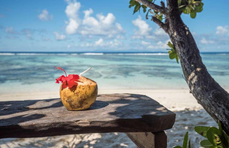 Eine Kokosnuss mit einer Blume darin sitzt auf einem Holztisch am Strand