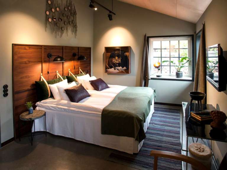 Ein Hotelzimmer mit Doppelbett, Nachttisch, Fenster und Fernseher.