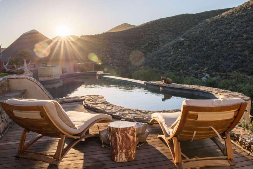 Zwei Holzstühle sitzen auf einem Deck neben einem Pool