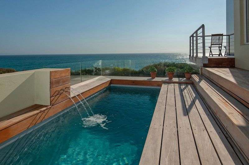 Ein kleiner Pool mit einem Wasserfall auf einem Holzdeck mit Blick auf den Ozean