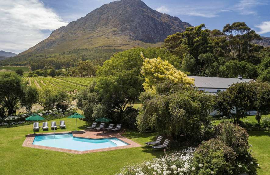 Ein Pool mit Stühlen und Sonnenschirmen in einem Garten mit einem Berg im Hintergrund