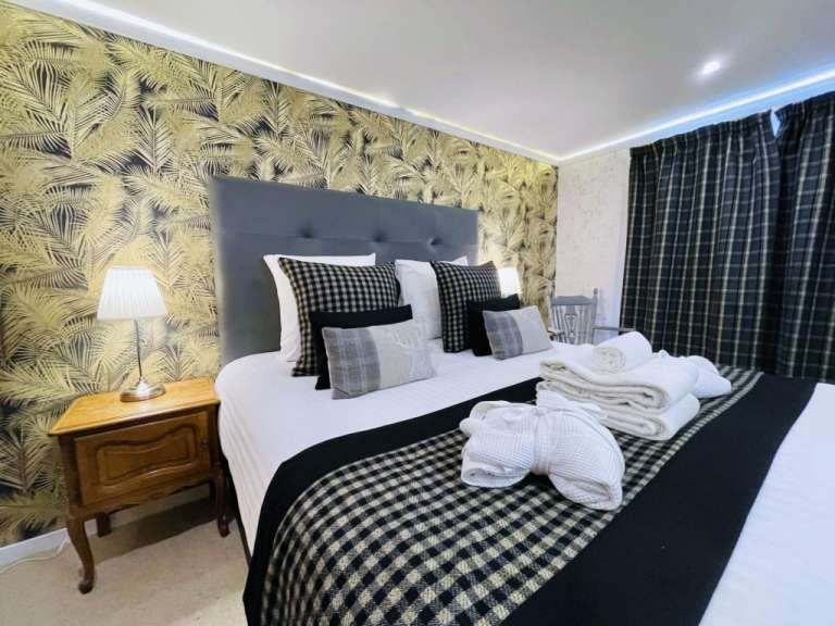 Das Bild zeigt ein Hotelzimmer mit einem großen Bett, das mit gemusterten Kissen und einer karierten Decke dekoriert ist.