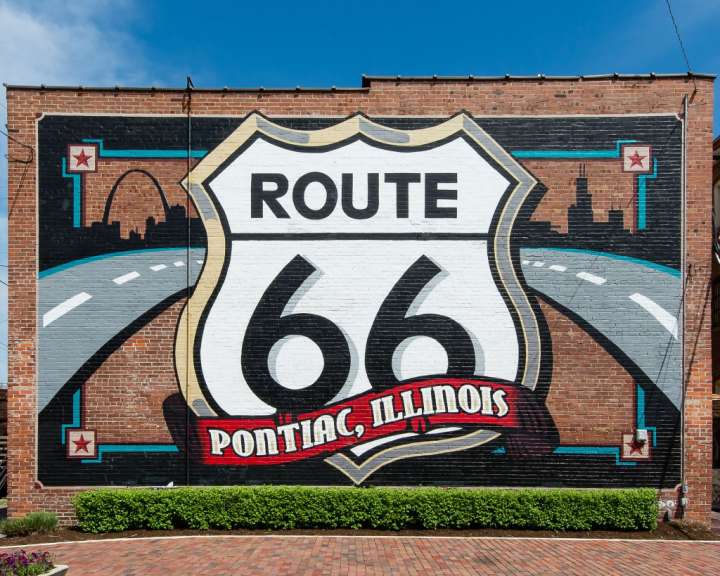 Ein großes Wandgemälde auf einer Backsteinwand zeigt das bekannte Route 66-Schild mit dem Schriftzug „Pontiac, Illinois“.