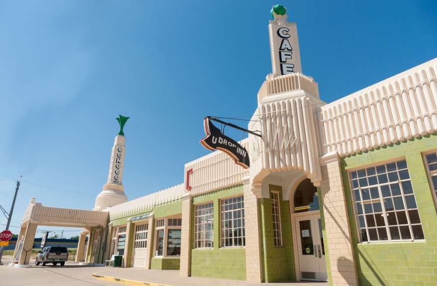 Das Bild zeigt das U-Drop Inn, ein historisches Art-déco-Gebäude in Shamrock, Texas, mit einer Tankstelle und einem Café.