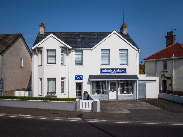 Ein weißes Gebäude mit der Aufschrift "Atlantic Antiques" und "B&B" steht neben anderen Häusern unter einem blauen Himmel.